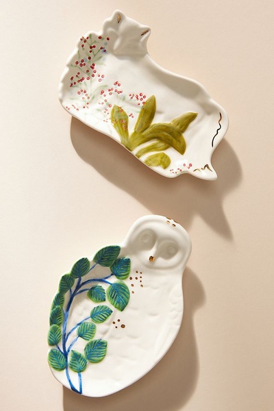 A high-angle product photograph showcasing two distinctively shaped ceramic dishes, one fox-themed and one owl-themed, arranged on a neutral beige background.