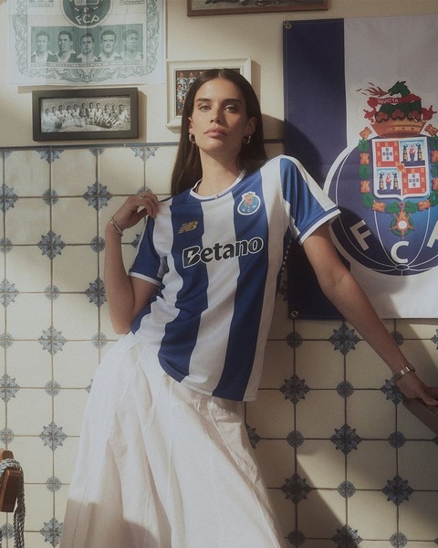 A portrait-style shot of a model wearing a branded blue and white striped football jersey in a classic, vintage-tiled interior setting.