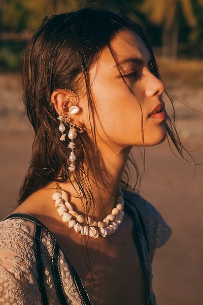 A high-end editorial shot featuring a model wearing a unique seashell necklace and a statement pearl earring in sunset lighting.