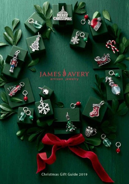 A top-down, flat-lay arrangement of silver jewelry charms displayed as a festive Christmas wreath on a dark green background with a red ribbon.
