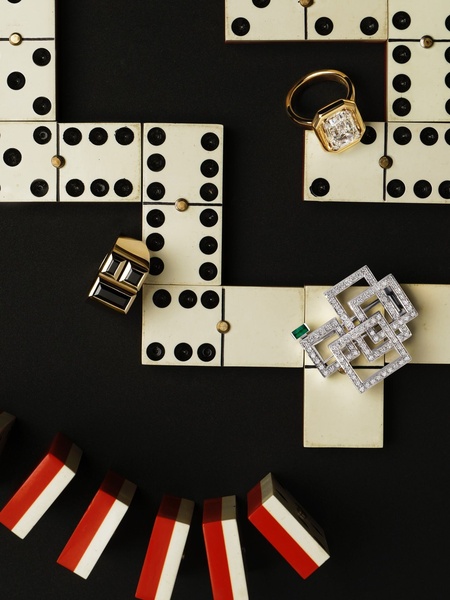 A high-end editorial display featuring an emerald-accented diamond brooch and gold rings arranged strategically on vintage-style dominoes.