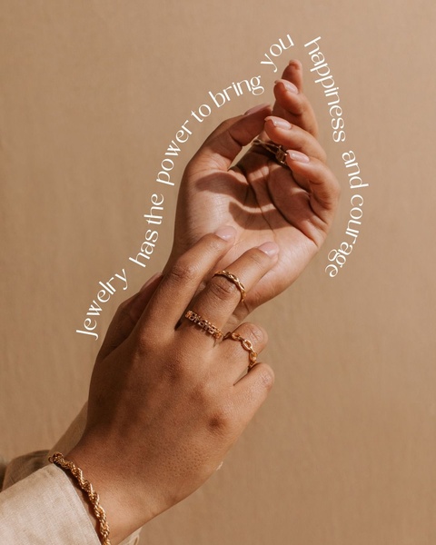 A close-up of a person's hands wearing gold rings and a bracelet against a neutral backdrop, featuring inspirational text about the power of jewelry.