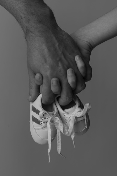 A grayscale close-up shot showing an adult hand holding a pair of tiny white infant shoes, conveying a sense of care and new beginnings.