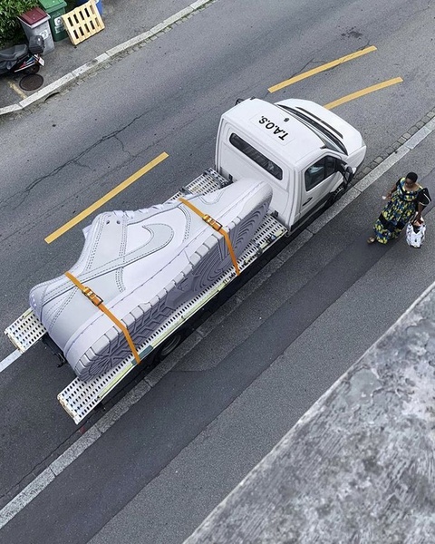 An oversized running shoe strapped to a flatbed truck creates a surreal, high-contrast visual for brand recall.