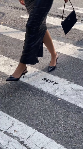 A high-fashion street photography shot capturing the movement of a person wearing heels, with the brand name integrated into the crosswalk markings.