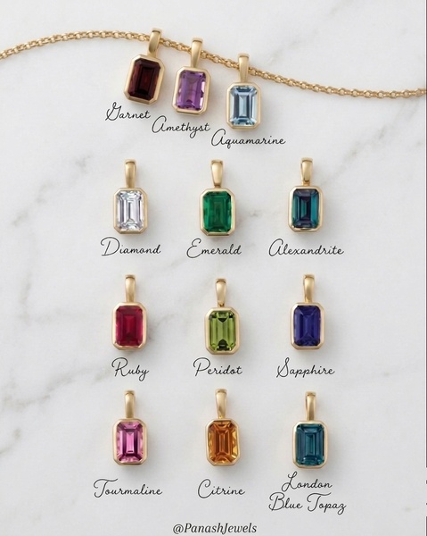 A clean, high-end product display showcasing twelve distinct gemstone pendants in gold settings against a white marble background.