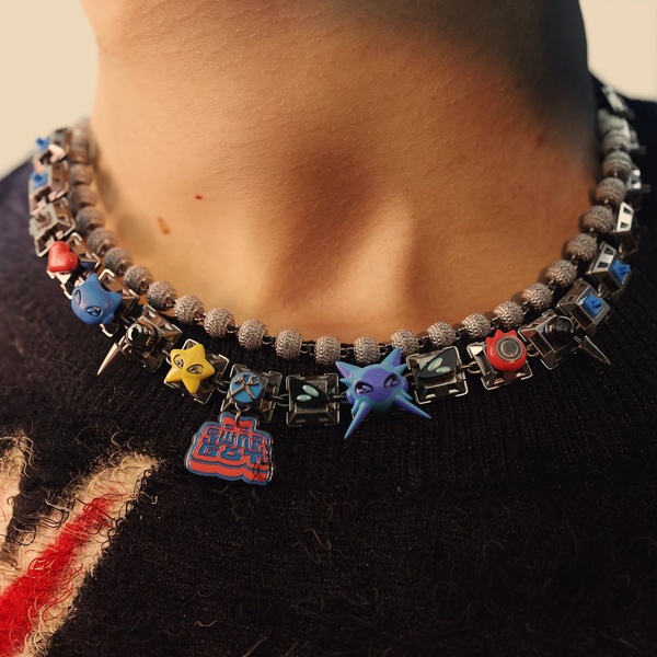 A close-up shot of a unique streetwear necklace featuring metal spikes, colorful charms, and a detailed beaded chain on a person.