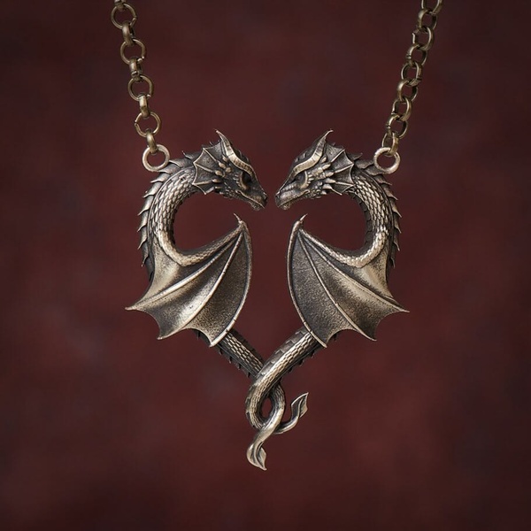 A close-up photograph of a metallic dragon necklace featuring two dragons positioned to form a heart shape against a deep red background.