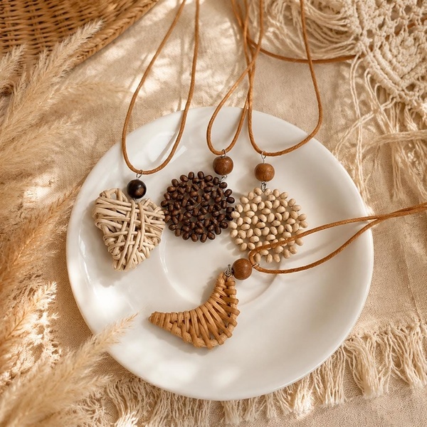 A close-up, top-down shot of four unique handmade pendant necklaces arranged on a clean white plate, surrounded by pampas grass for a soft, earthy aesthetic.