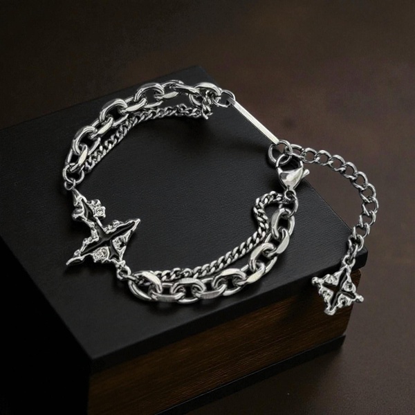 A high-contrast, clean product shot of a silver chain bracelet featuring cross motifs, laid elegantly on a black box.