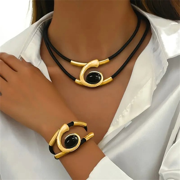 A close-up, high-fashion shot featuring a model wearing a coordinated black and gold necklace and bracelet set, emphasizing a modern minimalist aesthetic.