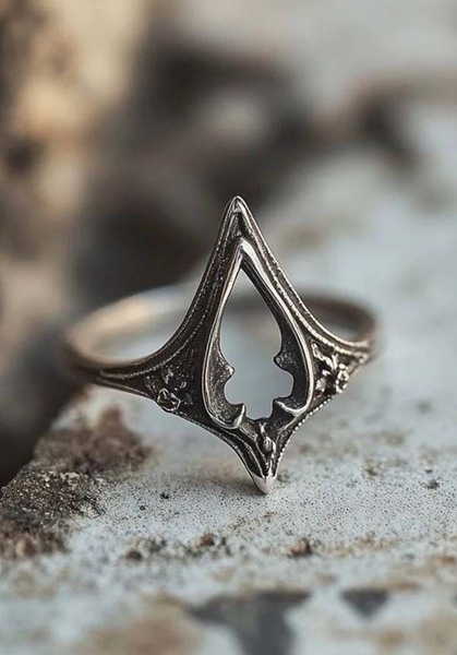 A close-up product shot of an intricate, metal ring featuring a diamond-shaped cutout design against a textured, neutral background.