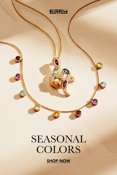 A high-end studio shot of a gold-chained necklace featuring multi-colored gemstones arranged in a serpentine shape on a warm, textured background.