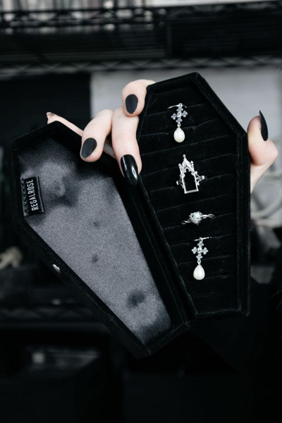 A close-up photograph showcasing a gothic-style jewelry ring set presented inside a velvet-lined coffin-shaped jewelry box.