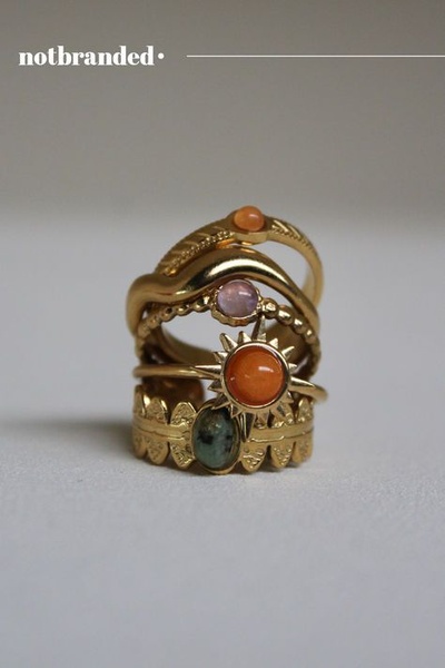 A close-up, high-detail photograph of five varied gold rings stacked vertically, featuring textured bands and colorful gemstone accents.