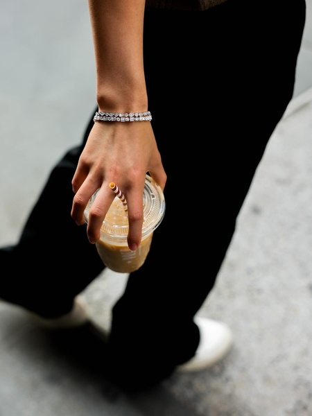 A close-up shot of a wrist wearing a sparkling tennis bracelet while holding a coffee, focusing on a relatable, high-end lifestyle moment.