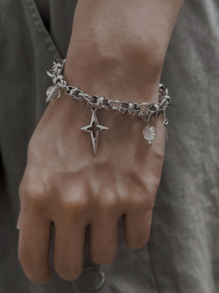 A sharp, close-up shot focusing on a silver charm bracelet featuring a star pendant and transparent crystal beads, worn against a neutral fabric background.