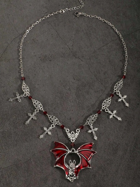 A high-contrast hero image of a silver bat necklace with red enamel wings, accented with small crosses and red beads against a dark textured background.