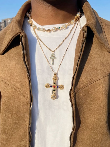 A close-up aesthetic shot of a model wearing a layered necklace set, highlighting the texture and detail of the gold-toned pendants against a simple white backdrop.