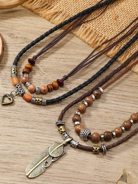 A close-up aesthetic shot featuring two layered beaded necklaces with heart and feather pendants, set against a natural wood and burlap background.