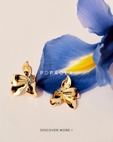 A close-up still life featuring gold flower-shaped earrings placed next to a vibrant blue iris petal, highlighting the jewelry's organic design.