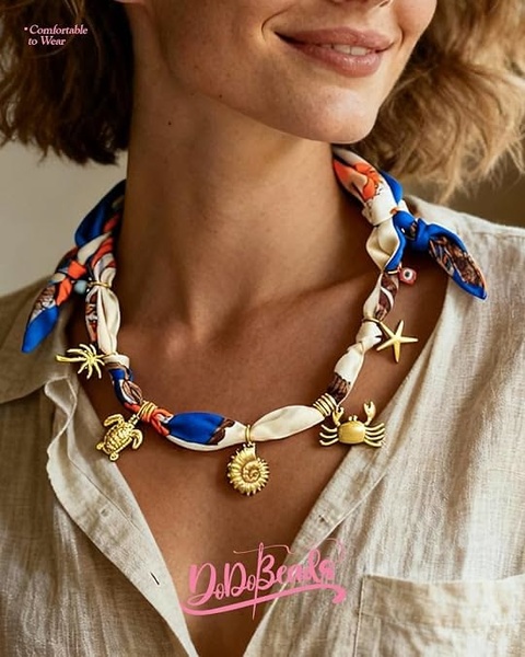 A close-up, warm-toned portrait featuring a stylish necklace made from a patterned silk scarf adorned with gold-toned sea-life charms.