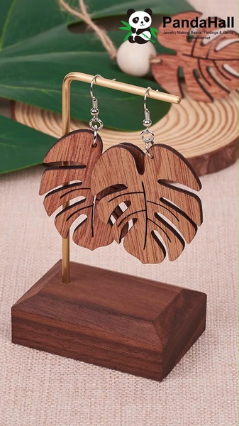 A high-quality 9:16 vertical product shot featuring wooden monstera leaf earrings displayed on a minimalist wooden stand.