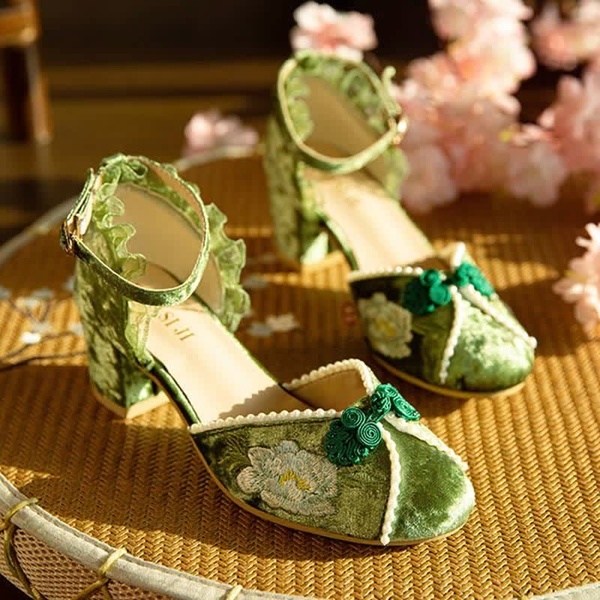 A high-angle product photography shot focusing on intricate floral embroidery and velvet textures of women's heels.
