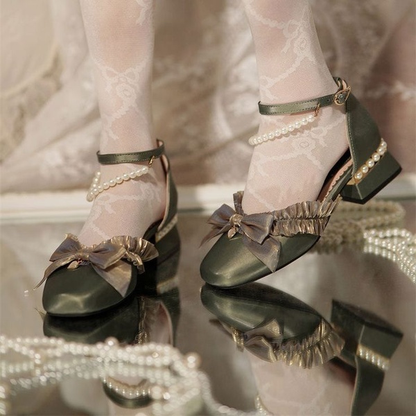 A close-up aesthetic shot of pearl-adorned olive satin ribbon heels reflecting on a mirrored surface, emphasizing texture and luxury.