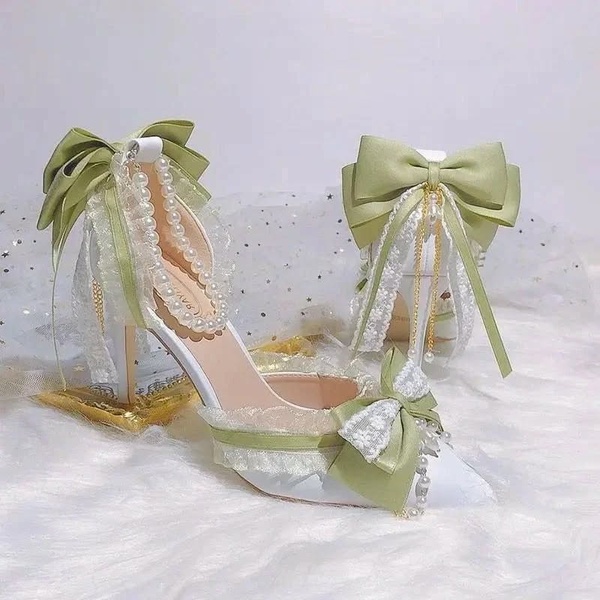 A high-end, 1:1 square-ratio product hero shot featuring sage green bridal heels adorned with lace, ribbon bows, and pearl accents.