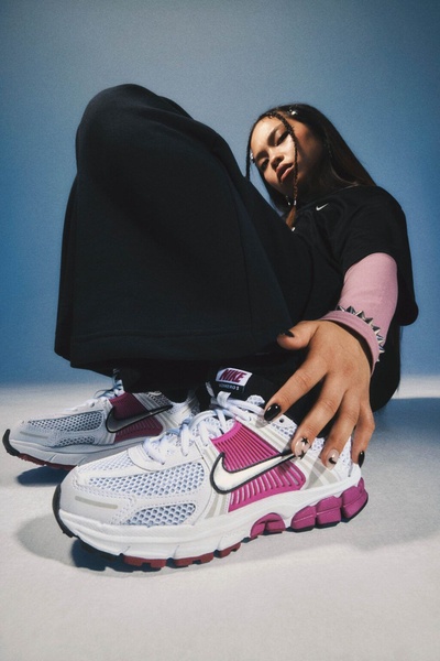 A close-up, low-angle lifestyle shot of a runner wearing high-contrast white and pink running shoes, focusing on the footwear's silhouette.