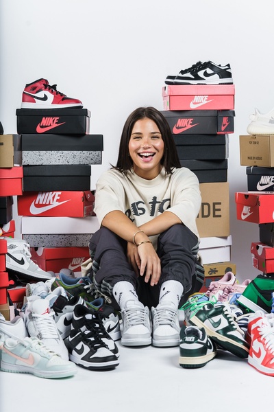 A vibrant, human-centered creative featuring a subject surrounded by a towering stack of sneaker boxes, emphasizing high-volume product variety.