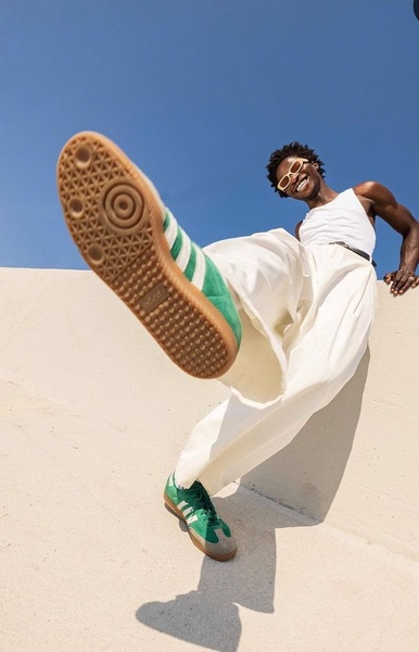 A high-energy, low-angle shot of a person wearing bright green sneakers, creating a dynamic sense of movement and scale against a clear blue sky.