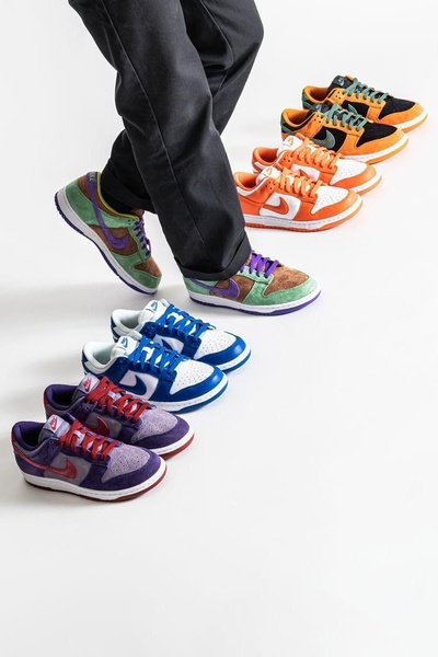 A high-quality studio shot of a person wearing one pair of patterned sneakers while surrounded by a cascading line of color-coordinated shoe variations.