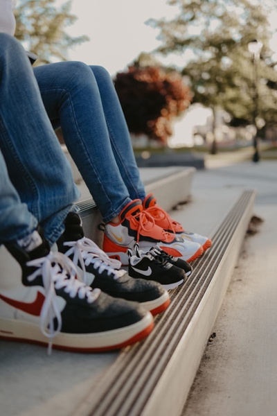 A low-angle lifestyle shot focusing on different sizes and styles of athletic footwear worn by people sitting on steps.