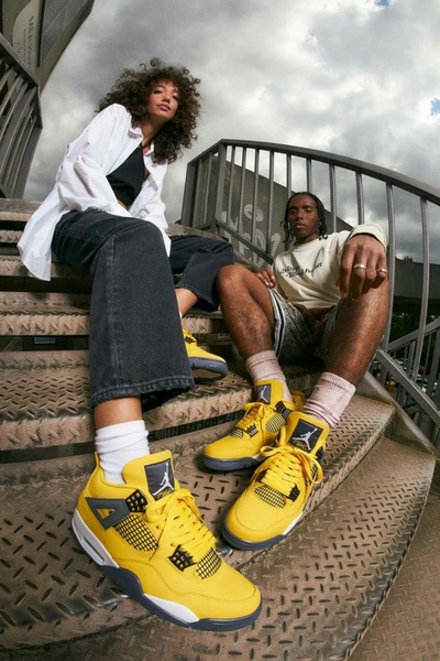 A high-angle, fisheye-style lifestyle creative capturing two models seated on stairs, emphasizing the bold yellow sneakers in the foreground.