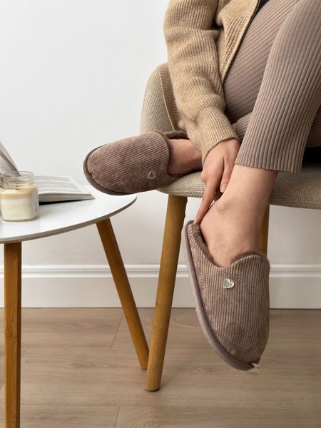 A close-up, natural light shot of a person wearing ribbed slippers while sitting in a chair, emphasizing the texture and home comfort.