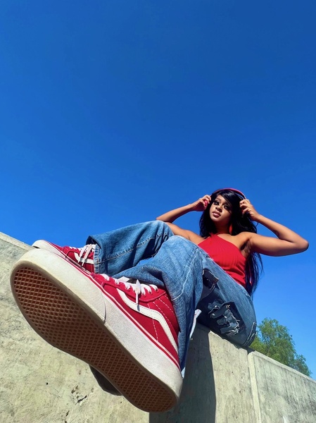 A high-energy, low-angle shot of a model wearing red sneakers against a clear blue sky, emphasizing the product's profile.