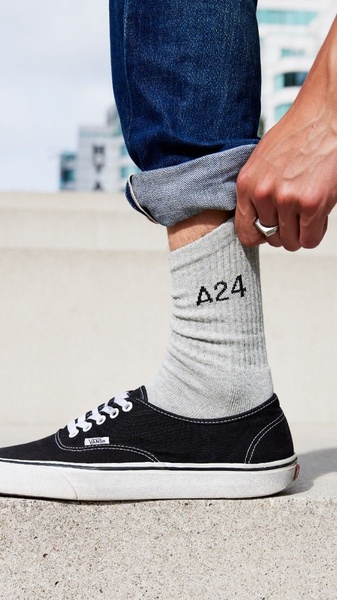 A close-up lifestyle photograph showing a model wearing gray crew socks with black text paired with denim and black canvas sneakers.