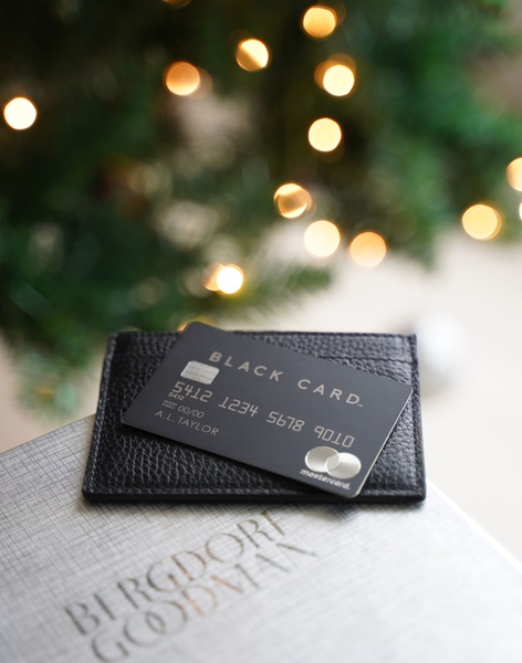 A high-end credit card displayed on a leather cardholder against a blurred festive background of warm holiday lights.