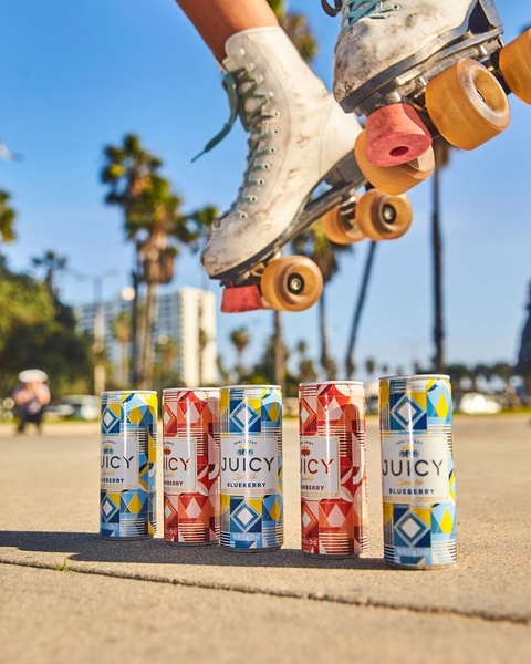 A high-action shot featuring a roller skater mid-air above a lineup of colorful sparkling beverage cans, emphasizing movement and summer aesthetics.