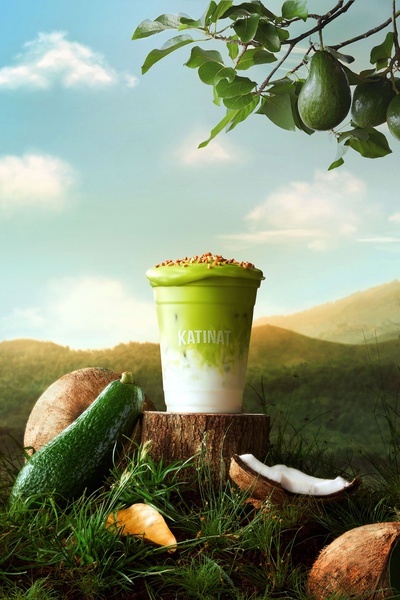 A high-quality product shot of an avocado coconut smoothie cup placed in a forest setting with raw ingredients.