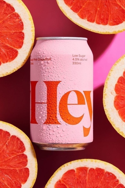 A high-contrast, professional product shot featuring a single grapefruit tonic can surrounded by halved pink grapefruits, set against a vibrant magenta background.
