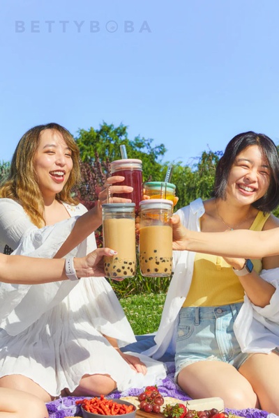 A bright, outdoor lifestyle shot capturing a group of friends cheering with their bubble tea drinks on a sunny day.