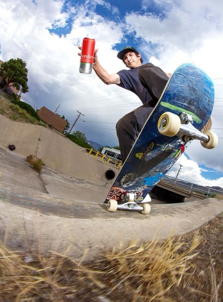 An action-oriented shot featuring an energy drink can held by a skateboarder performing a trick in an outdoor concrete skate bowl.