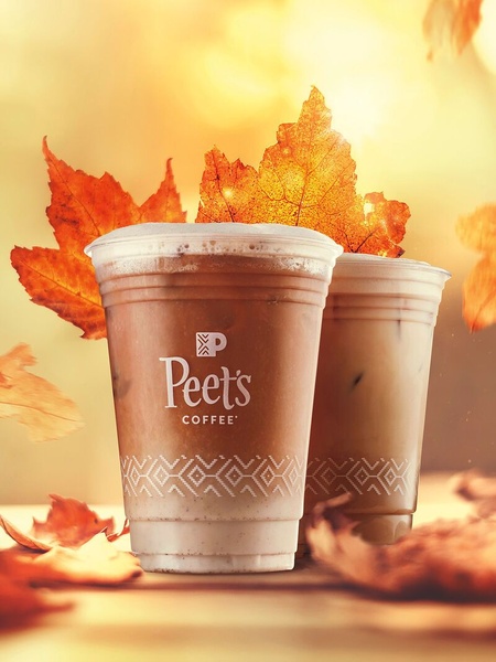 This creative displays two iced coffee beverages front and center against a backdrop of falling autumn leaves, leveraging seasonal aesthetics to evoke a specific mood.