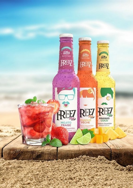 The creative displays three variations of a flavored drink on a wooden beach table, surrounded by fresh fruit and mint, set against a blurred sunny seaside background.