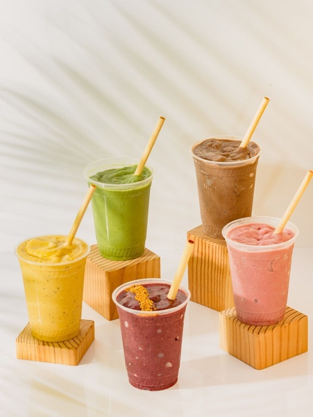 A high-quality product photography shot featuring five different colorful smoothies arranged on wooden blocks against a textured, neutral background.