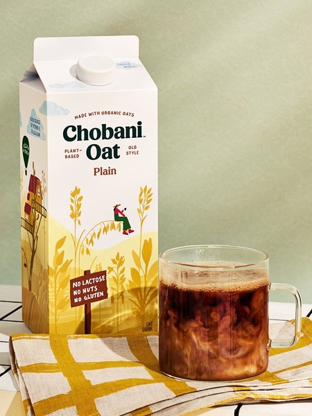 A high-contrast, vertical product shot of oat milk paired with a warm morning coffee, highlighting organic origins through artistic packaging and cozy settings.