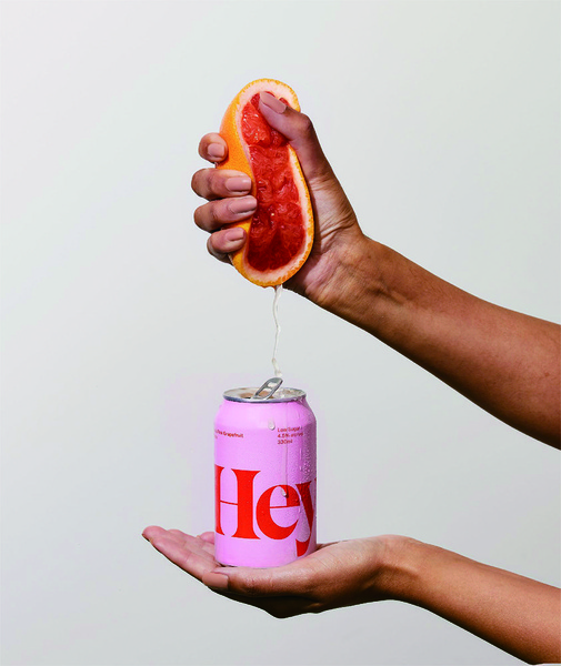 A high-contrast, minimalist shot showing a hand squeezing a fresh grapefruit directly into a branded seltzer can.